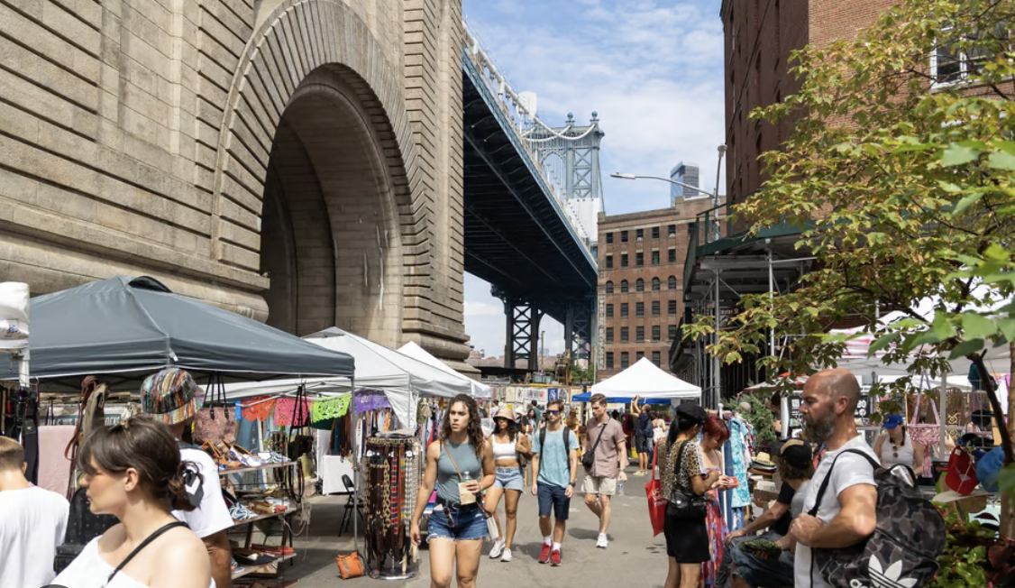Busy open-air market under a bridge with vendor tents and shoppers